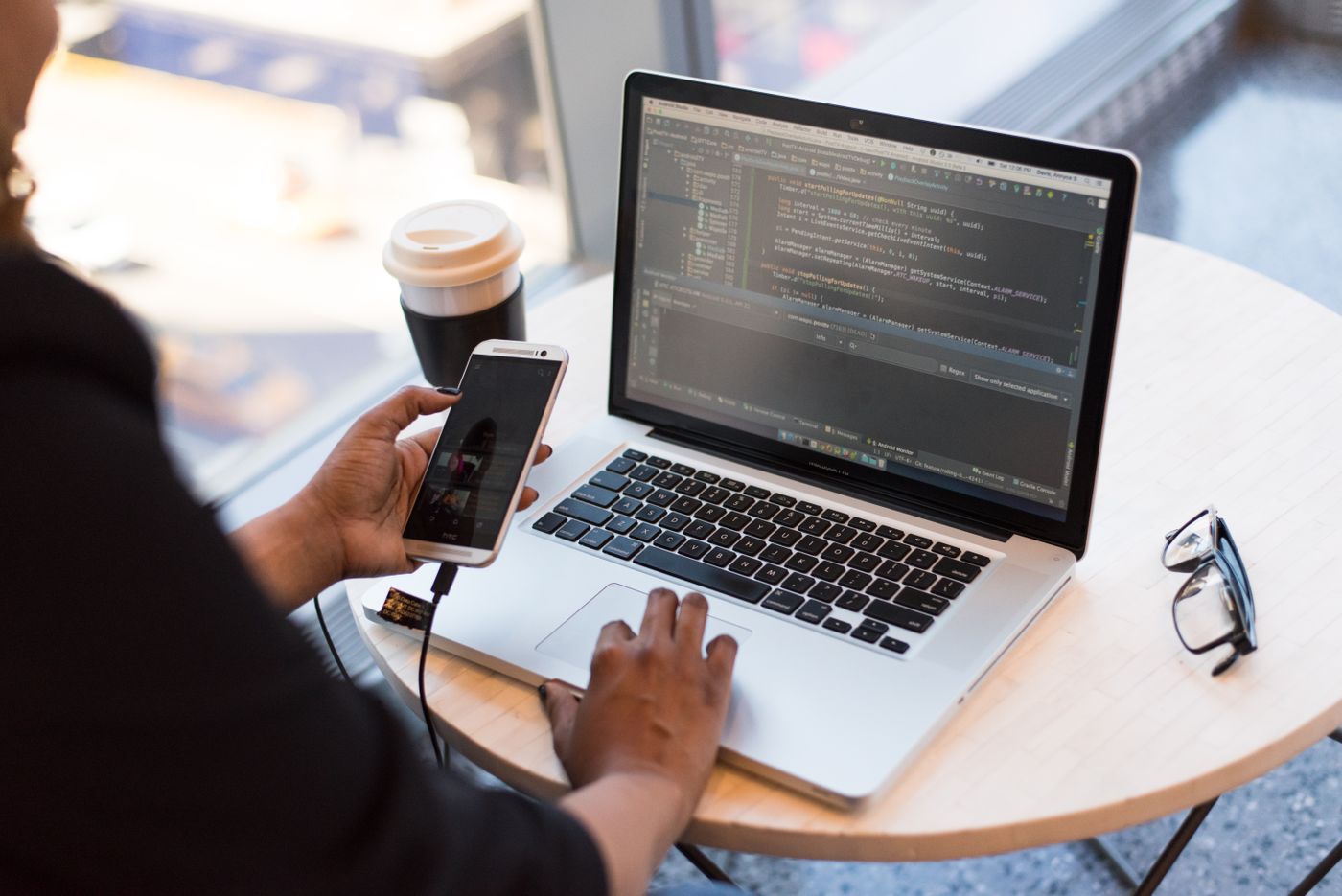 Black developer coding on laptop with phone